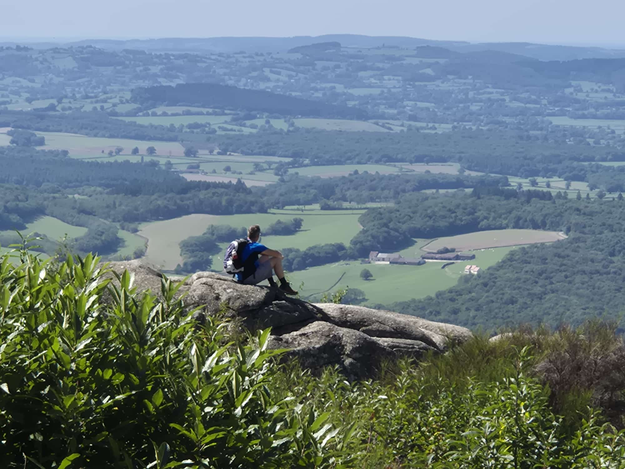 Wandelaar rust uit op een rotsblok. Op de achtergrond het landschap van de Morvan